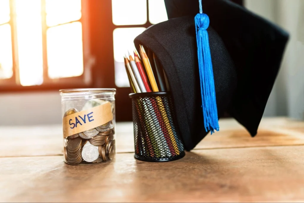 Graduation cap beside a pencil holder and a glass jar labeled “SAVE” filled with coins, symbolizing budgeting for a veterinary medicine degree. Vetucore LLC helps future veterinarians prepare financially for their education.