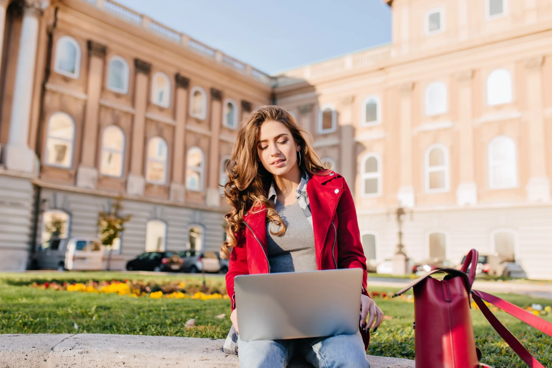 Young female student working on her laptop outside a university building, preparing her veterinary school application with Vetucore LLC's expert guidance.
