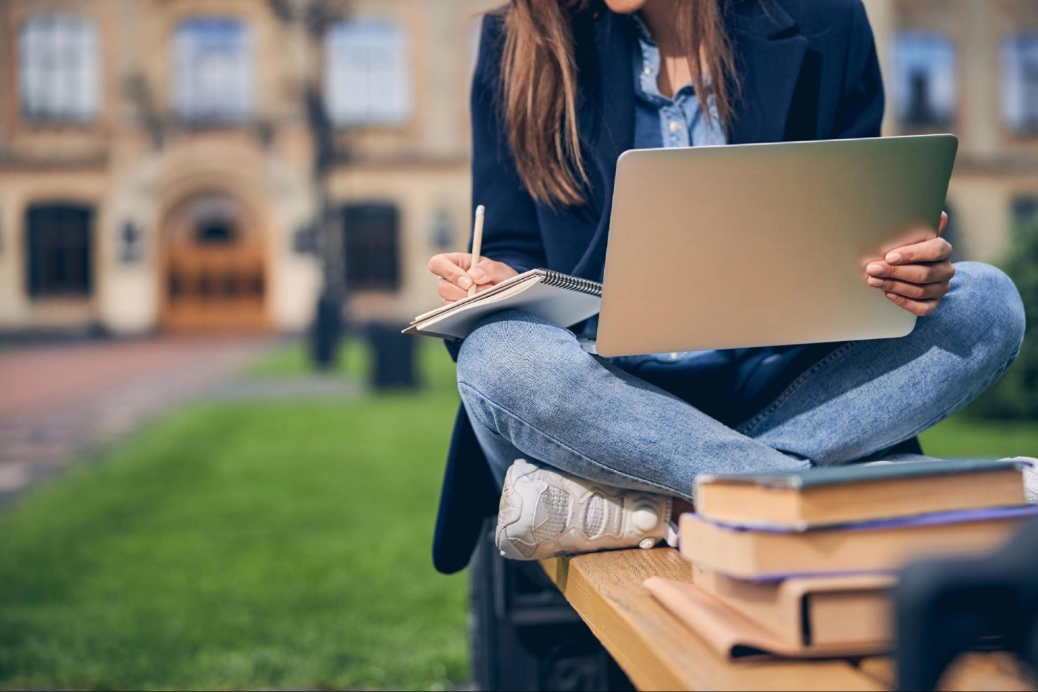Student preparing veterinary school application while studying on campus lawn with laptop and books — Vetucore LLC veterinary consulting.